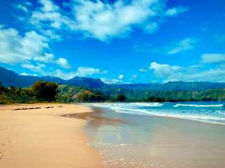 Die Hanalei Bay ist die längste Bucht der Insel Kauai. Im Hintergrund befinden sich grüne und hohe Berge.