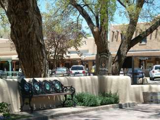 Taos Plaza ist ein kleiner Park mit Bäumen und Bänken, der von verschiedenen Geschäften umgeben ist.